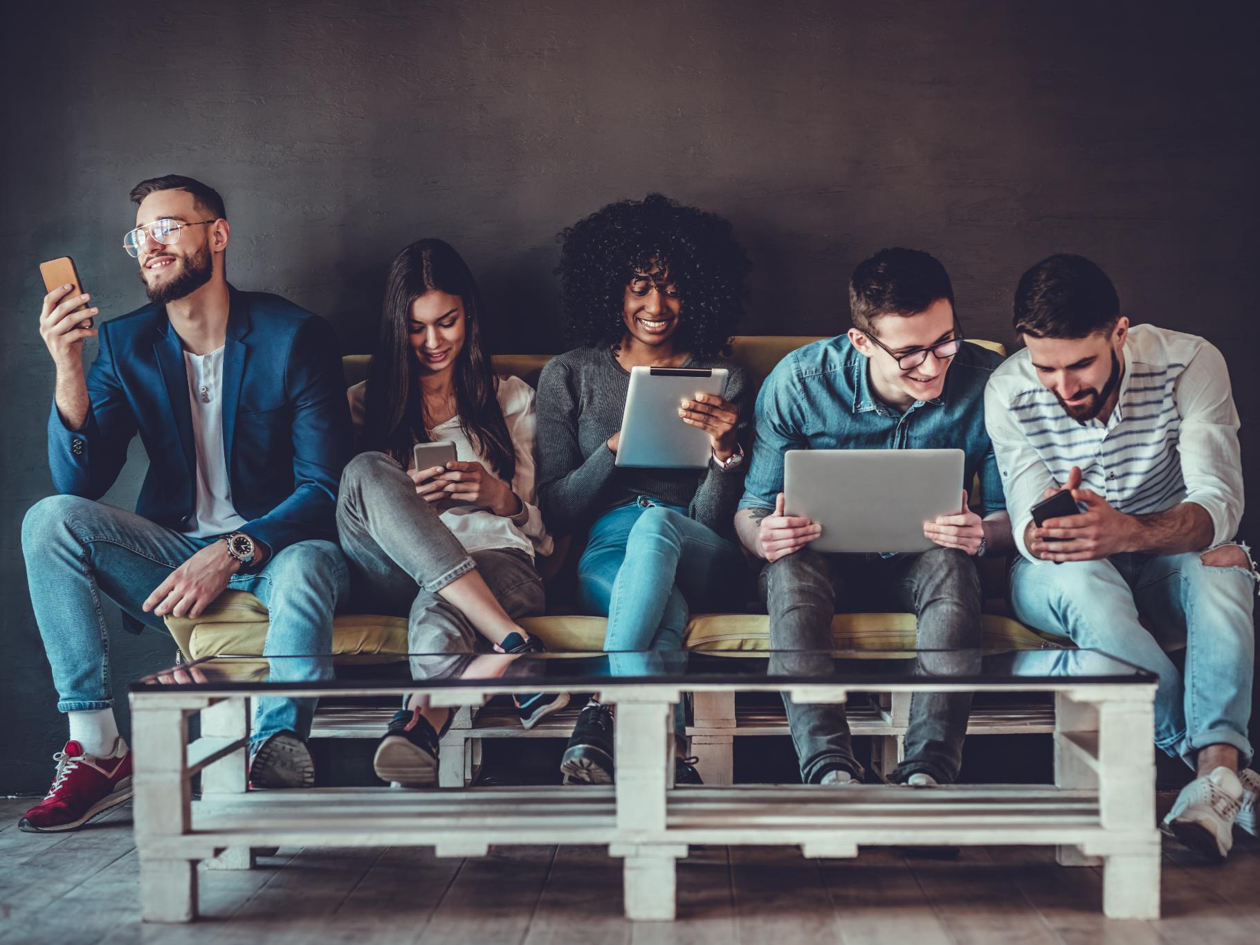 5 people sitting on couch looking at electronics